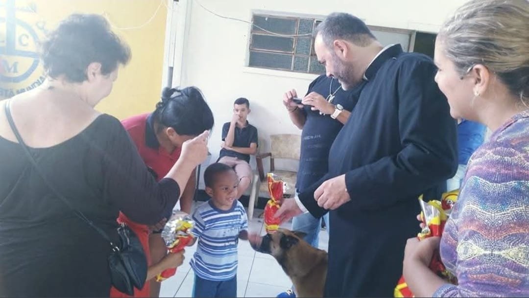 Criança recebe presente do sacerdote e das voluntárias