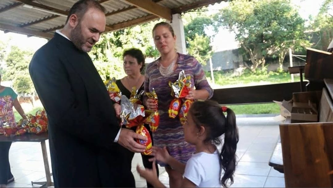 Sacerdote entrega presentes ao lado das voluntárias